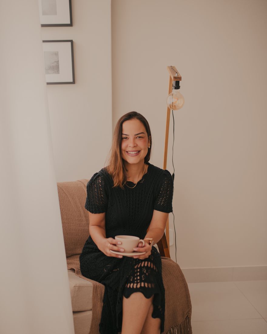 Taís Faria, criadora do método B.T.S, sentada com uma xícara de café ao lado de uma luminária de filamento